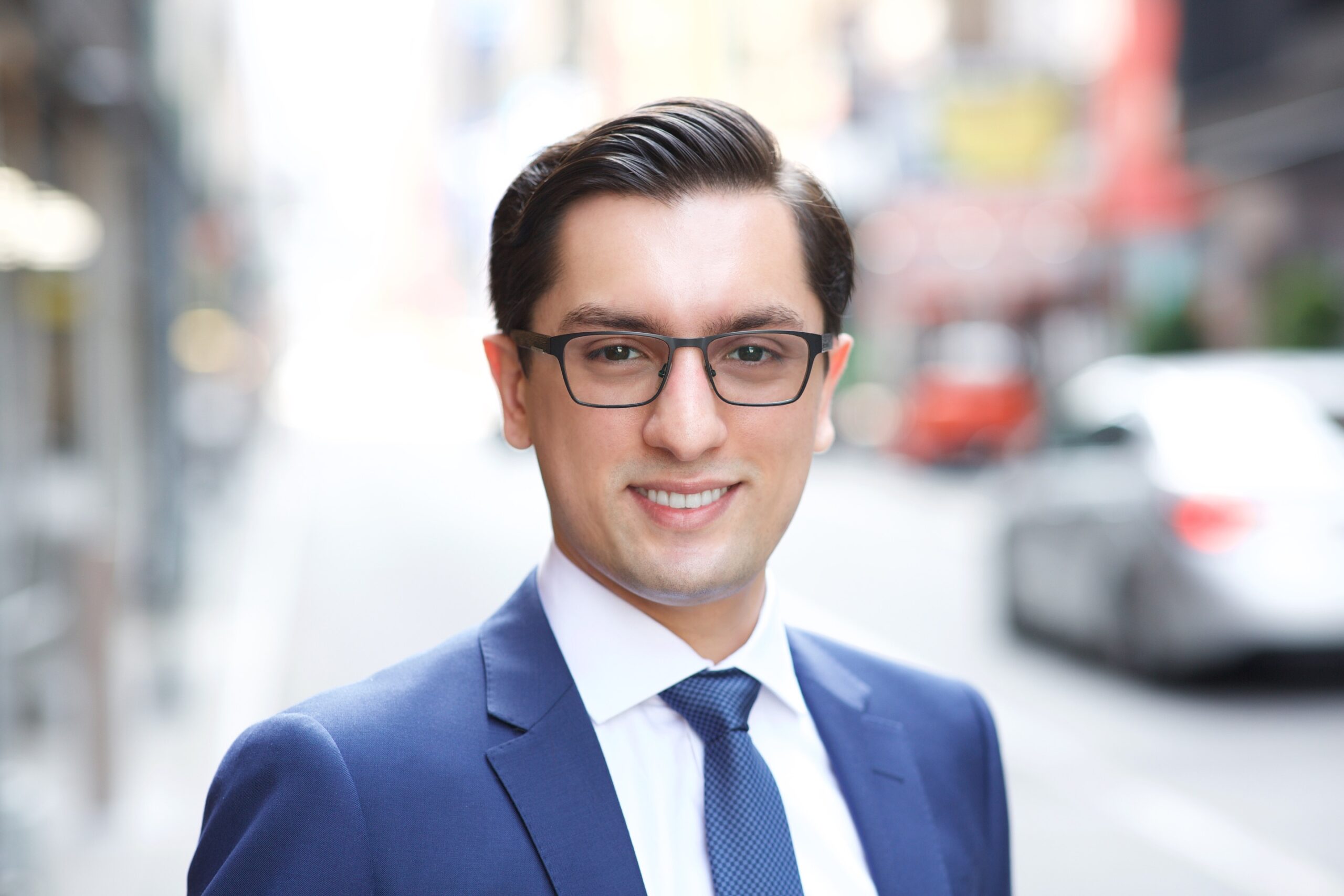 Business headshot NYC — man in glasses and blue suit, outdoor city street background