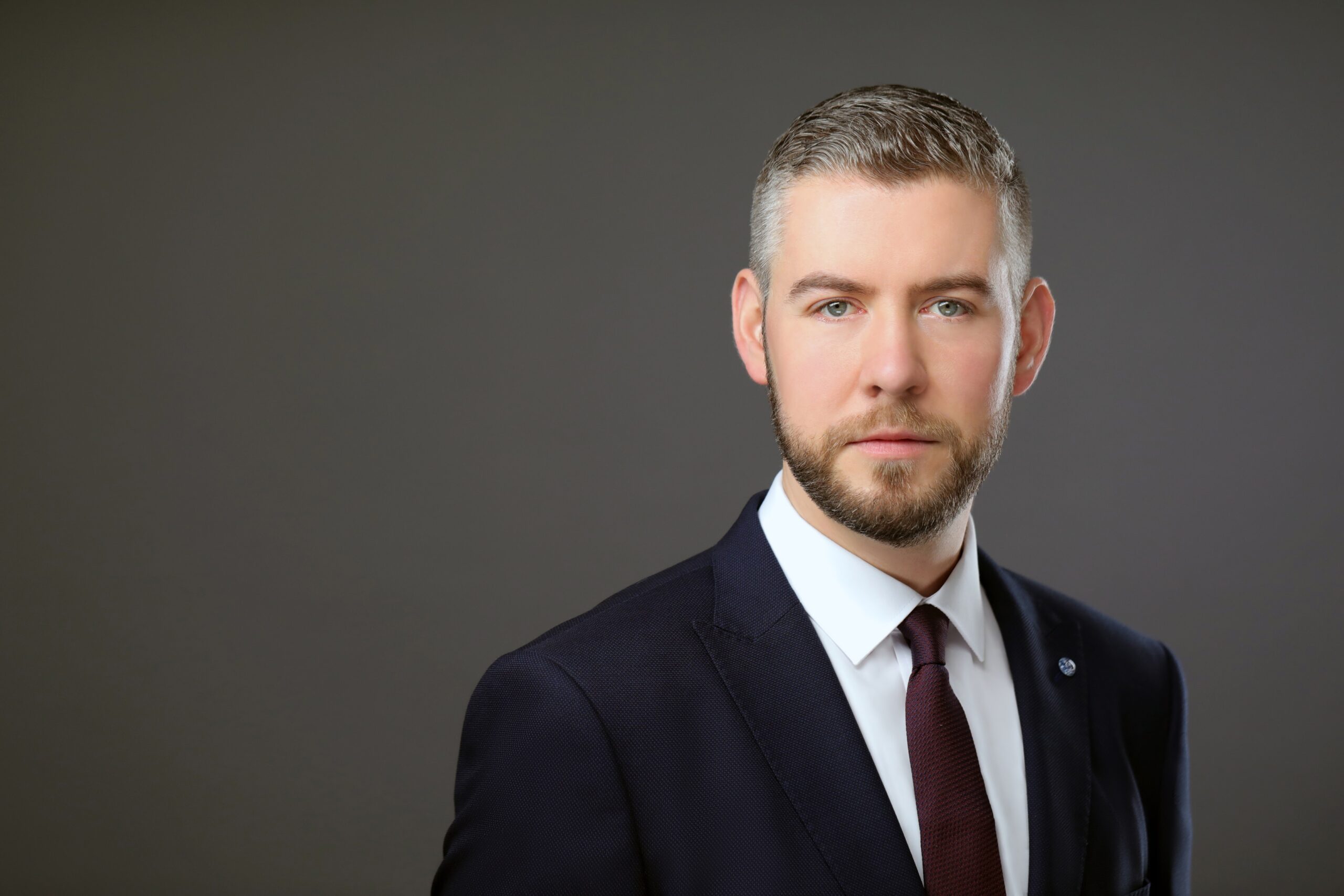 Business headshot NYC — bearded executive in navy suit and burgundy tie, dark studio backdrop