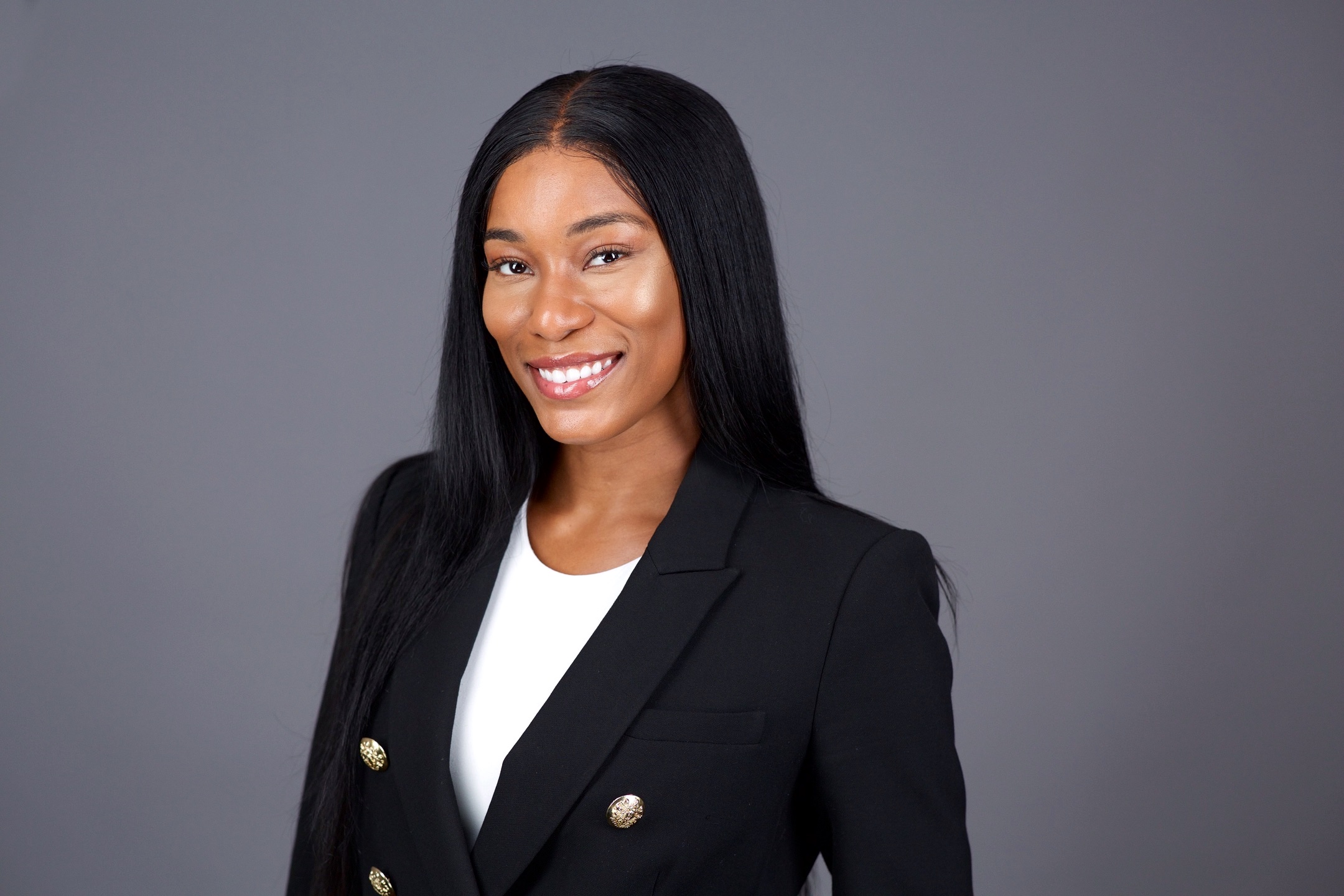 Business headshot NYC — smiling woman in black double-breasted blazer, grey studio backdrop