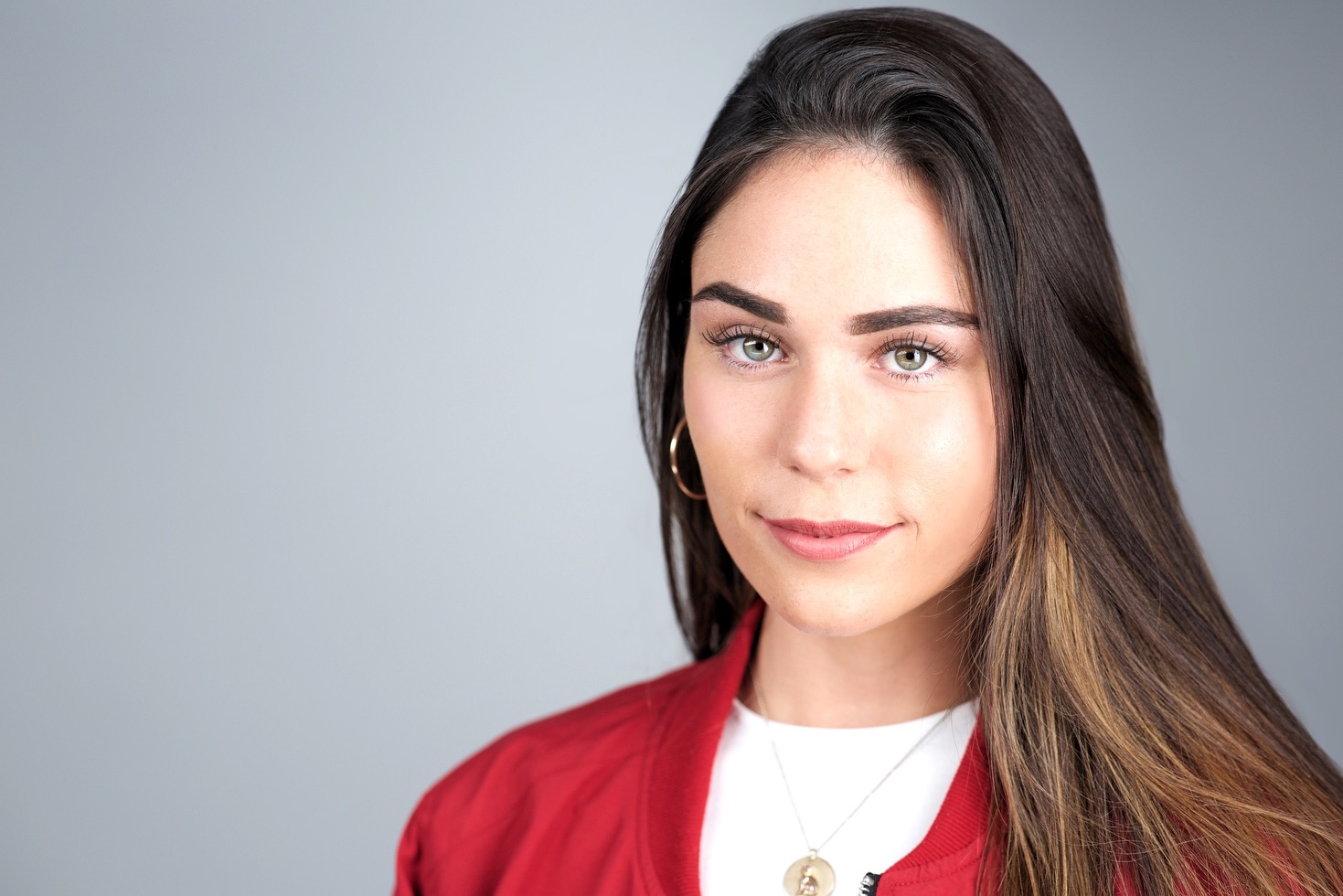 Business headshot NYC — young woman in red blazer, grey studio backdrop