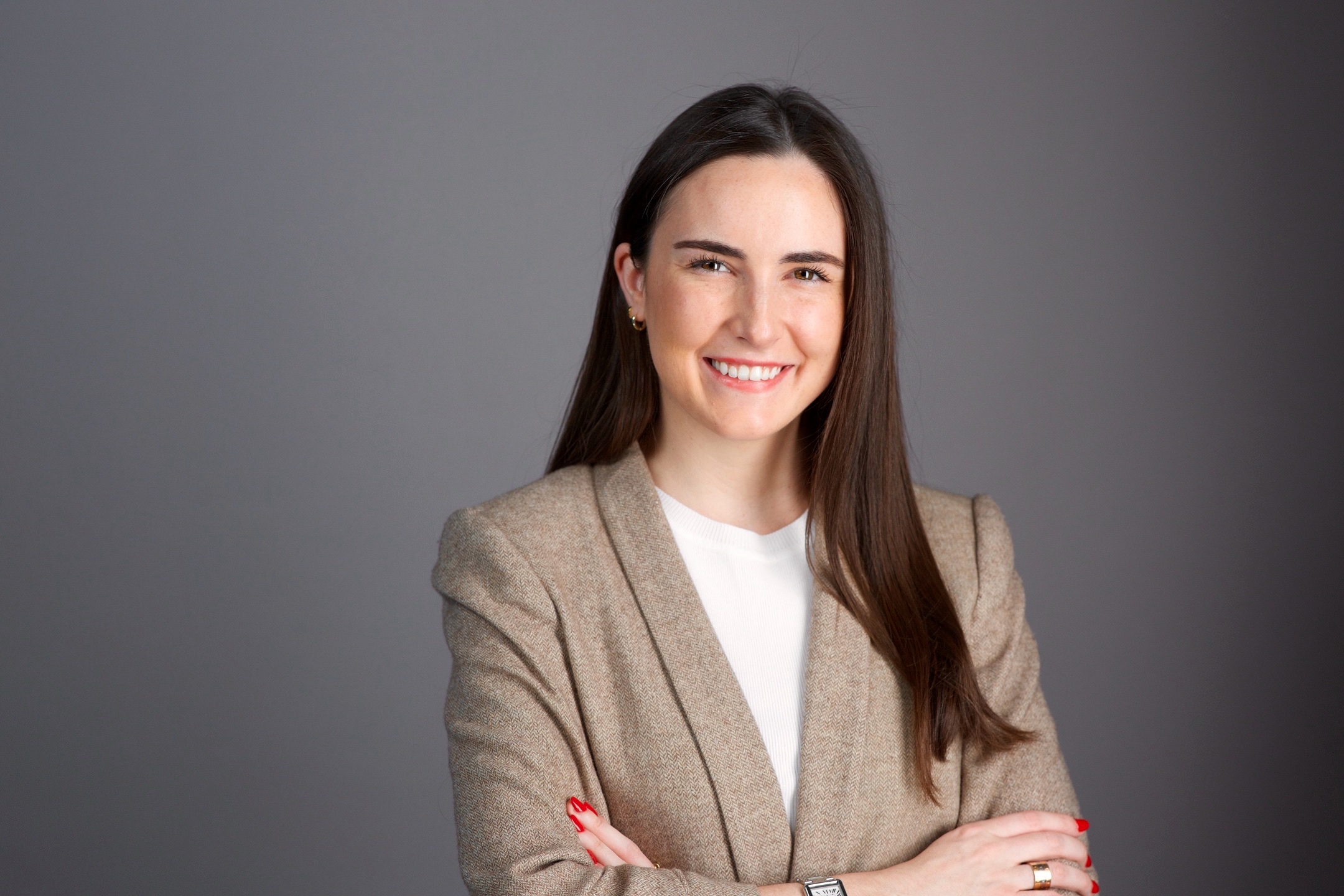 Corporate headshot NYC — smiling woman in beige blazer with arms crossed, grey backdrop