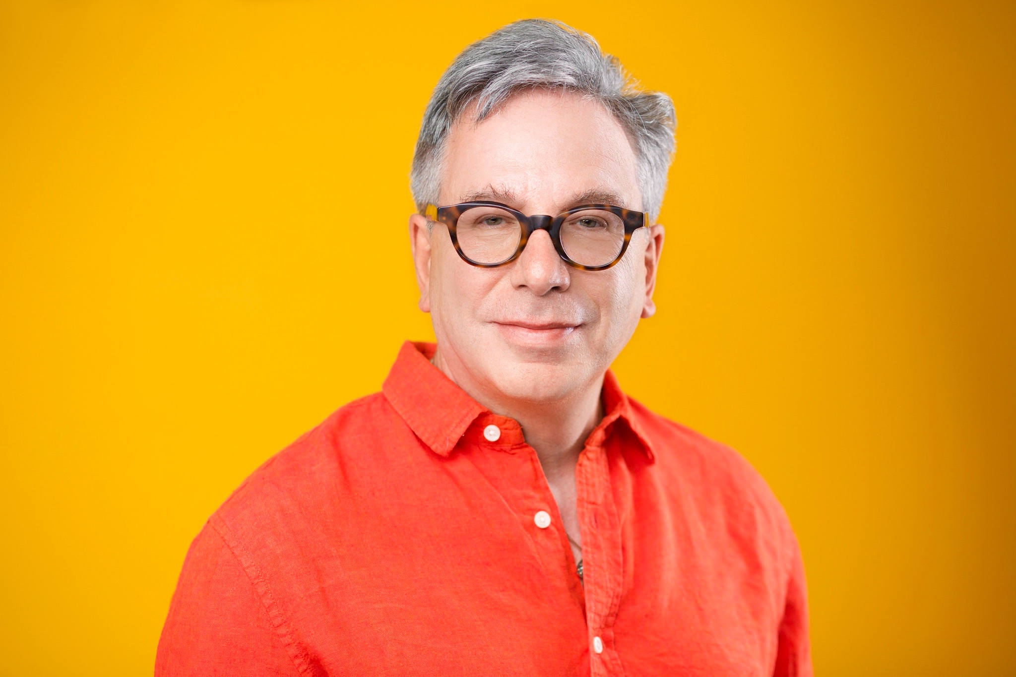 Creative headshot NYC — man in orange shirt and glasses on yellow background